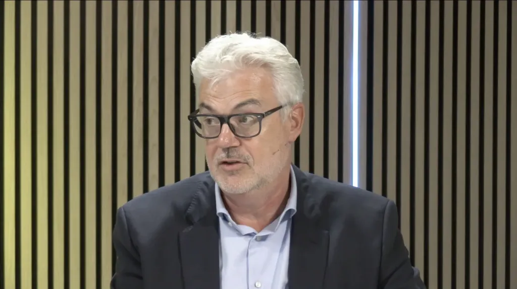 Spreker met bril aan tafel tijdens het webinar