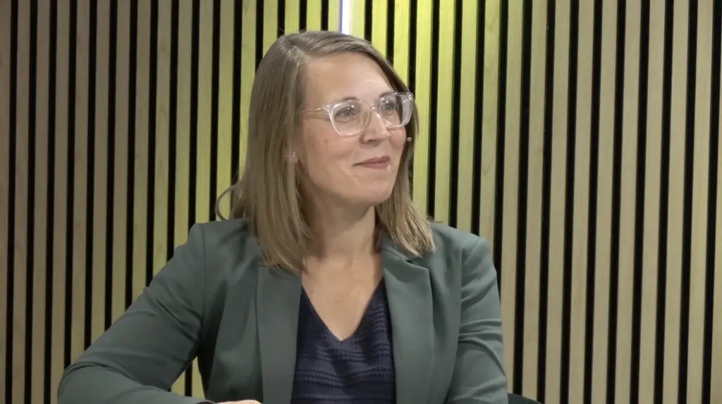 Spreker luistert glimlachend aan tafel tijdens het webinar