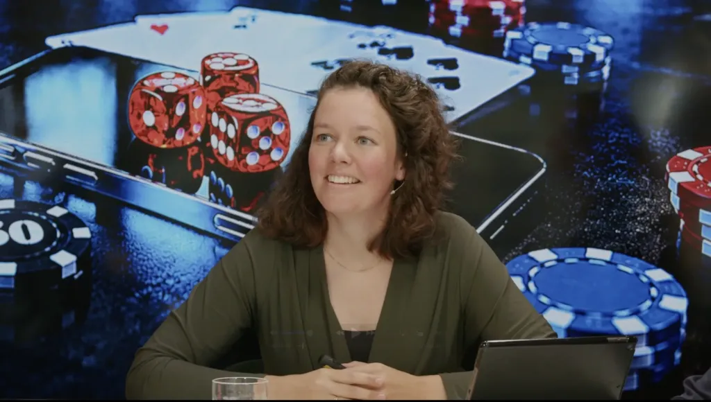 Deelnemer aan tafel tijdens het webinar, met speelkaarten, dobbelstenen en fiches op het scherm erachter