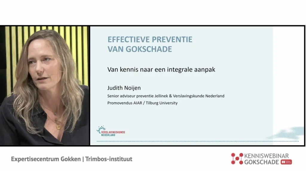 Spreker naast de slide Effectieve preventie van gokschade, met de naam van de organisatie in beeld